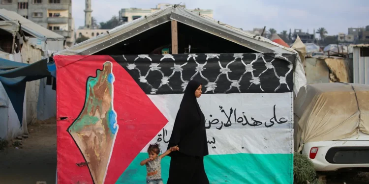 Una mujer palestina camina con un niño junto a una bandera palestina en el campamento de Bureij, en el centro de la Franja de Gaza, el 22 de septiembre de 2025. (Foto de Eyad BABA / AFP)