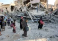Palestinos desplazados llevan sus pertenencias mientras caminan entre los escombros de un edificio destruido durante un ataque israelí nocturno en el barrio de Rimal, en la ciudad de Gaza, el 13 de septiembre de 2025 (Omar AL-QATTAA / AFP)