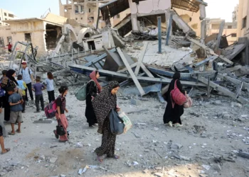 Palestinos desplazados llevan sus pertenencias mientras caminan entre los escombros de un edificio destruido durante un ataque israelí nocturno en el barrio de Rimal, en la ciudad de Gaza, el 13 de septiembre de 2025 (Omar AL-QATTAA / AFP)