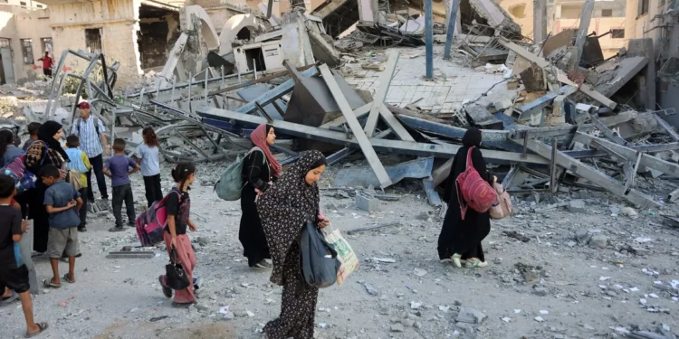 Palestinos desplazados llevan sus pertenencias mientras caminan entre los escombros de un edificio destruido durante un ataque israelí nocturno en el barrio de Rimal, en la ciudad de Gaza, el 13 de septiembre de 2025 (Omar AL-QATTAA / AFP)