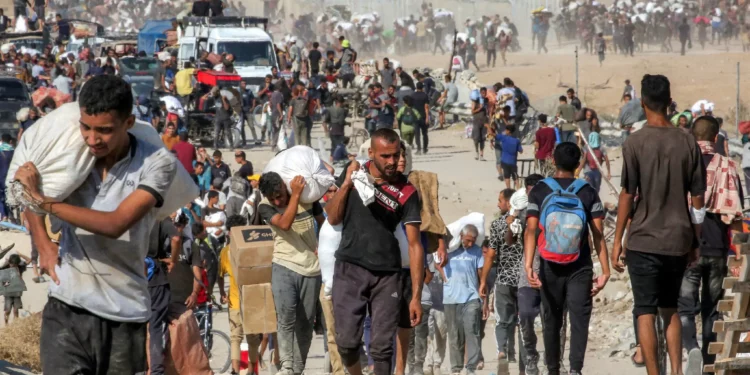 La gente camina con bolsas de ayuda humanitaria que recibieron en un centro de distribución administrado por la Fundación Humanitaria de Gaza (GHF), respaldada por Estados Unidos e Israel, mientras cruzan el corredor de Netzarim en el centro de la Franja de Gaza, el 22 de agosto de 2025. (Eyad BABA / AFP)