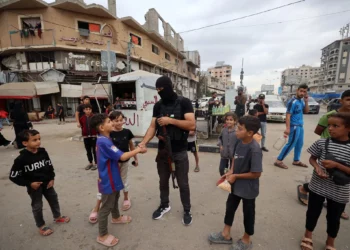 Un miembro de las fuerzas de seguridad interna leales al grupo terrorista palestino Hamás saluda a jóvenes gazatíes en el campo de refugiados de Nuseirat, en el centro de la Franja de Gaza, el 12 de octubre de 2025. (Eyad BABA / AFP)