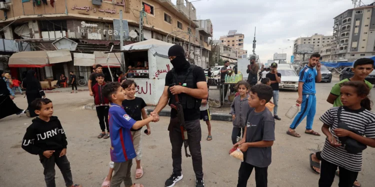 Un miembro de las fuerzas de seguridad interna leales al grupo terrorista palestino Hamás saluda a jóvenes gazatíes en el campo de refugiados de Nuseirat, en el centro de la Franja de Gaza, el 12 de octubre de 2025. (Eyad BABA / AFP)