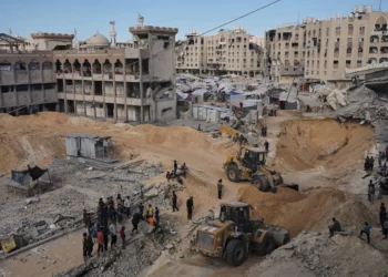 Palestinos observan a miembros del grupo terrorista Hamás mientras buscan los cuerpos de los rehenes en una zona de la ciudad de Hamad, Khan Younis, en el sur de la Franja de Gaza, el sábado 18 de octubre de 2025. (Foto AP/Jehad Alshrafi)
