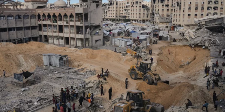 Palestinos observan a miembros del grupo terrorista Hamás mientras buscan los cuerpos de los rehenes en una zona de la ciudad de Hamad, Khan Younis, en el sur de la Franja de Gaza, el sábado 18 de octubre de 2025. (Foto AP/Jehad Alshrafi)