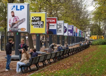 Personas disfrutan del clima otoñal junto a algunos de los carteles electorales de 26 de los 27 partidos políticos que participan en las elecciones generales del 29 de octubre en La Haya, Países Bajos, el miércoles 22 de octubre de 2025. (Foto AP/Peter Dejong)