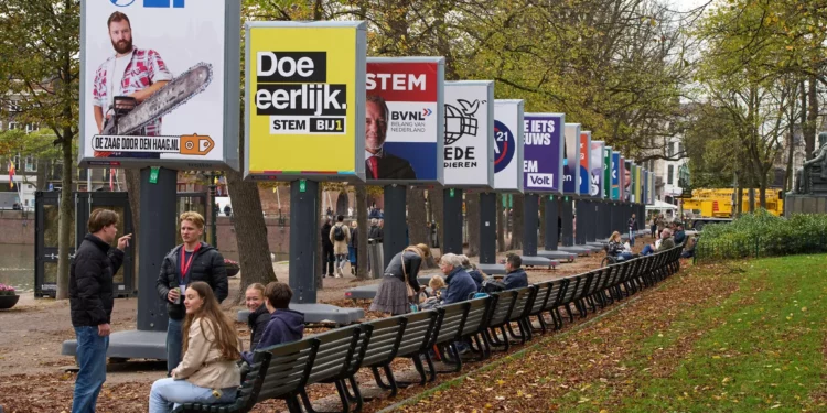 Personas disfrutan del clima otoñal junto a algunos de los carteles electorales de 26 de los 27 partidos políticos que participan en las elecciones generales del 29 de octubre en La Haya, Países Bajos, el miércoles 22 de octubre de 2025. (Foto AP/Peter Dejong)