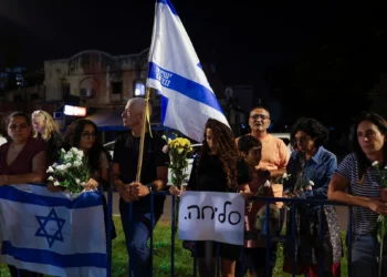 La gente lleva flores y banderas israelíes a la llegada de vehículos que transportan los cuerpos de cuatro rehenes entregados frente al Centro Nacional de Medicina Forense en Tel Aviv el 13 de octubre de 2025. (Foto de Jalaa MAREY / AFP)