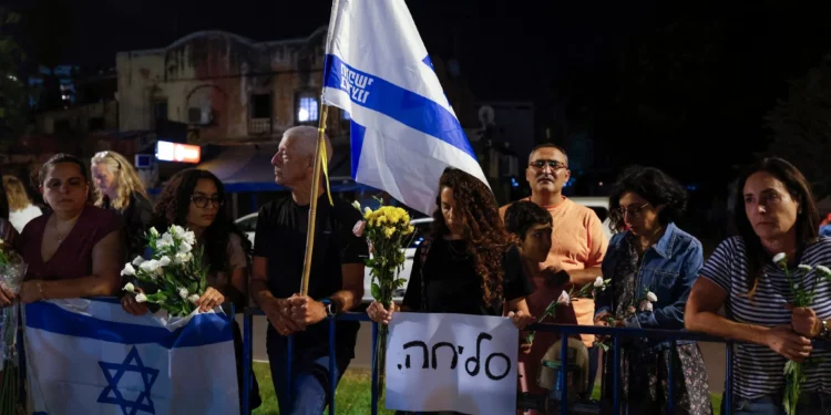 La gente lleva flores y banderas israelíes a la llegada de vehículos que transportan los cuerpos de cuatro rehenes entregados frente al Centro Nacional de Medicina Forense en Tel Aviv el 13 de octubre de 2025. (Foto de Jalaa MAREY / AFP)