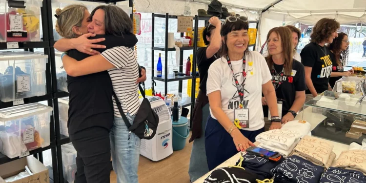 Dana Felz-Russo, a la izquierda, y otros voluntarios que venden mercancías en la Plaza de los Rehenes de Tel Aviv celebran un acuerdo para traer de vuelta a los 48 cautivos restantes el 9 de octubre de 2025 (Ben Sales/Times of Israel)