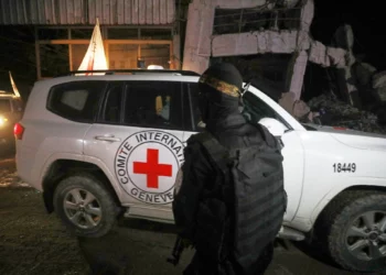 Un hombre armado, vestido con el uniforme de las Brigadas al-Qassam, el ala militar de Hamás, monta guardia mientras vehículos de la Cruz Roja, que supuestamente transportan ataúdes con los cuerpos de cuatro rehenes muertos, salen de un almacén con destino a Israel, en la ciudad de Gaza, el martes 14 de octubre de 2025. (Foto AP/Yousef Al Zanoun)