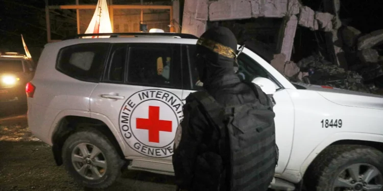 Un hombre armado, vestido con el uniforme de las Brigadas al-Qassam, el ala militar de Hamás, monta guardia mientras vehículos de la Cruz Roja, que supuestamente transportan ataúdes con los cuerpos de cuatro rehenes muertos, salen de un almacén con destino a Israel, en la ciudad de Gaza, el martes 14 de octubre de 2025. (Foto AP/Yousef Al Zanoun)