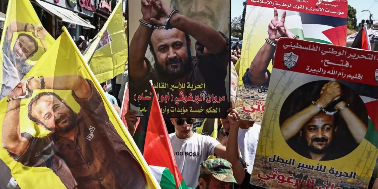 Manifestantes levantan banderas y carteles que representan a Marwan Barghouti, destacado miembro del partido Fatah y el terrorista palestino de más alto perfil encarcelado por Israel, durante una marcha en su apoyo en la ciudad de Ramallah, el 19 de agosto de 2025. (Zain JAAFAR / AFP)