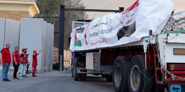 Miembros de la Media Luna Roja Egipcia vigilan los camiones con ayuda humanitaria a su entrada al cruce de Rafah, entre Egipto y la Franja de Gaza, tras el acuerdo de alto el fuego entre Israel y Hamás, el 12 de octubre de 2025. (AP/Mohamed Arafat)