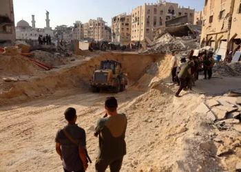 La gente observa cómo los palestinos usan una excavadora para cavar profundamente en el suelo, según se informa, buscando cadáveres en Jan Yunis, en el sur de la Franja de Gaza, el 17 de octubre de 2025 (Omar AL-QATTAA / AFP)