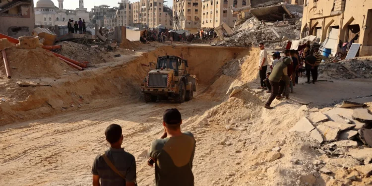 La gente observa cómo los palestinos usan una excavadora para cavar profundamente en el suelo, según se informa, buscando cadáveres en Jan Yunis, en el sur de la Franja de Gaza, el 17 de octubre de 2025 (Omar AL-QATTAA / AFP)