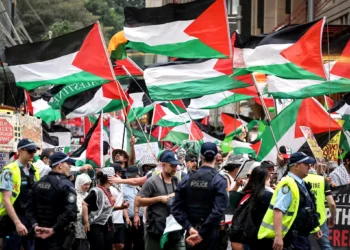Agentes de policía de Nueva Gales del Sur observan a manifestantes propalestinos que portan banderas y pancartas mientras marchan durante una manifestación en Sídney el 12 de octubre de 2025. (Foto de DAVID GRAY / AFP)