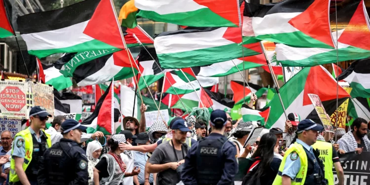 Agentes de policía de Nueva Gales del Sur observan a manifestantes propalestinos que portan banderas y pancartas mientras marchan durante una manifestación en Sídney el 12 de octubre de 2025. (Foto de DAVID GRAY / AFP)
