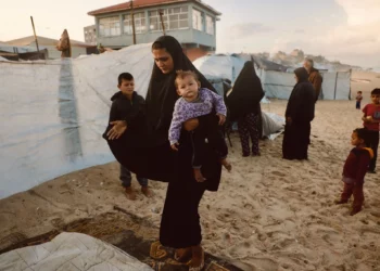 Una mujer palestina lleva a su hijo mientras se refugia de la lluvia en un campamento improvisado que alberga a palestinos desplazados en Deir al-Balah, en el centro de la Franja de Gaza, el 25 de noviembre de 2025 (Bashar Taleb / AFP)