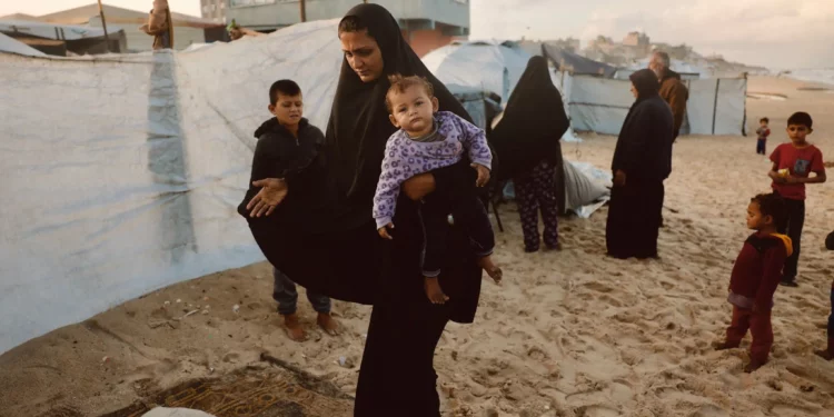 Una mujer palestina lleva a su hijo mientras se refugia de la lluvia en un campamento improvisado que alberga a palestinos desplazados en Deir al-Balah, en el centro de la Franja de Gaza, el 25 de noviembre de 2025 (Bashar Taleb / AFP)