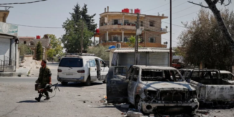 Un miliciano druso que porta una ametralladora pasa junto a un automóvil calcinado tras los enfrentamientos sectarios en la ciudad de Sweida, Siria, de mayoría drusa, el 25 de julio de 2025. (Foto AP/Omar Sanadiki)
