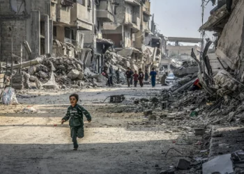 Un niño palestino corre junto a edificios destruidos en la guerra de Gaza, en Jan Yunis, sur de la Franja de Gaza, 6 de noviembre de 2025. (Abed Rahim Khatib/Flash90)