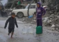 Un niño descalzo camina bajo la lluvia cargando una garrafa de agua de plástico en el barrio de Sheikh Radwan de la ciudad de Gaza, el 14 de noviembre de 2025. (Foto AP/Jehad Alshrafi)
