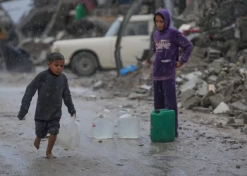 Un niño descalzo camina bajo la lluvia cargando una garrafa de agua de plástico en el barrio de Sheikh Radwan de la ciudad de Gaza, el 14 de noviembre de 2025. (Foto AP/Jehad Alshrafi)