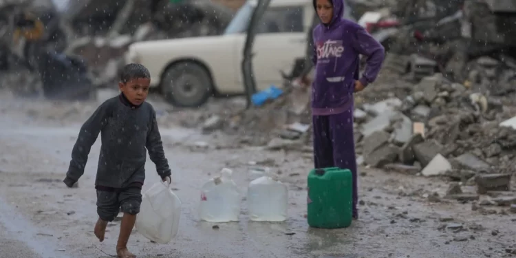 Un niño descalzo camina bajo la lluvia cargando una garrafa de agua de plástico en el barrio de Sheikh Radwan de la ciudad de Gaza, el 14 de noviembre de 2025. (Foto AP/Jehad Alshrafi)