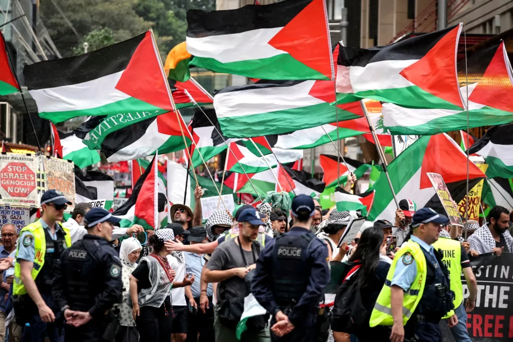 Agentes de policía de Nueva Gales del Sur observan a manifestantes propalestinos sostener banderas y pancartas mientras marchan durante una manifestación en Sídney el 12 de octubre de 2025. (DAVID GRAY / AFP)