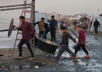 Palestinos desplazados caminan por senderos fangosos mientras un hombre y sus hijos cargan utensilios de cocina en un campamento en Jabalia, en el norte de la Franja de Gaza, el 7 de diciembre de 2025. (Foto AP/Jehad Alshrafi)