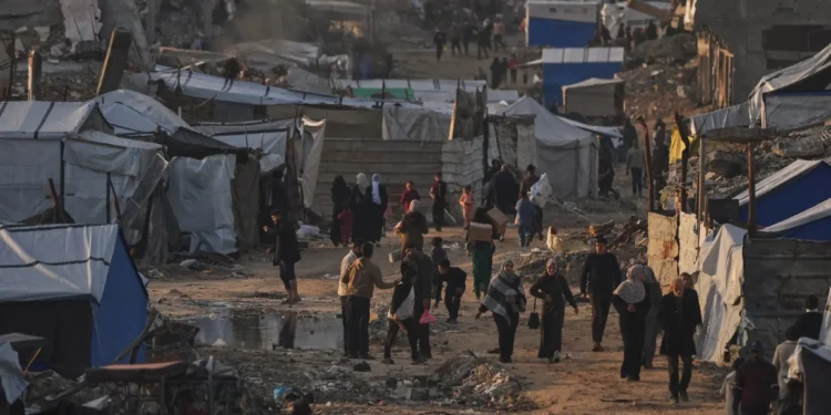 Palestinos caminan por una calle frente a un campamento de tiendas de campaña rodeado de edificios destruidos durante la guerra entre Israel y Hamás en la ciudad de Gaza, el 30 de diciembre de 2025. (AP/Jehad Alshrafi