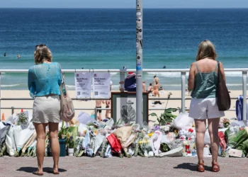 La gente se para frente a ofrendas florales dejadas en el paseo marítimo de Bondi Beach en Sídney el 18 de diciembre de 2025, para honrar a las víctimas del tiroteo terrorista que tuvo como objetivo un evento judío allí el 14 de diciembre de 2025. (DAVID GRAY / AFP)