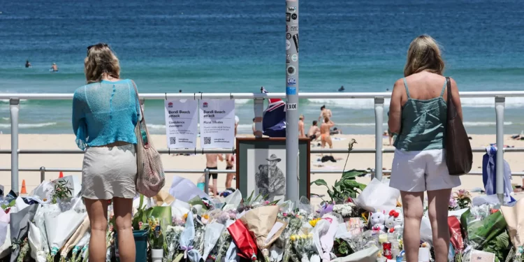 La gente se para frente a ofrendas florales dejadas en el paseo marítimo de Bondi Beach en Sídney el 18 de diciembre de 2025, para honrar a las víctimas del tiroteo terrorista que tuvo como objetivo un evento judío allí el 14 de diciembre de 2025. (DAVID GRAY / AFP)