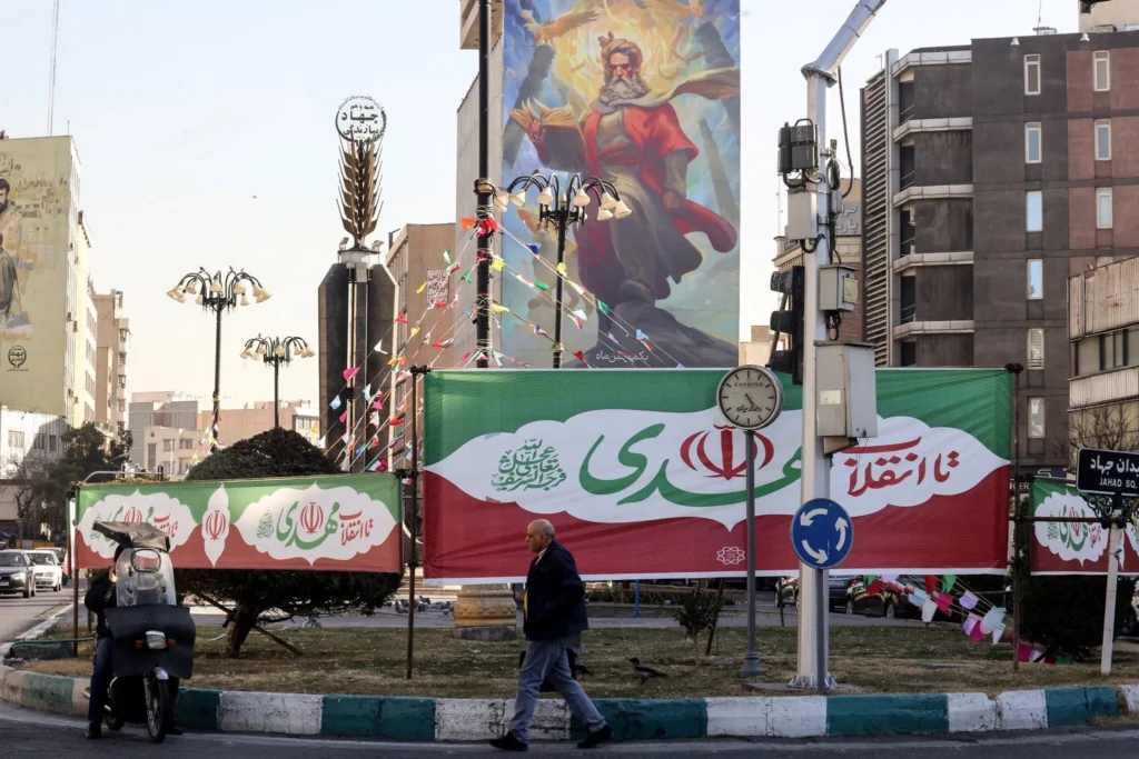 Banderas con los colores de la bandera iraní adornan una rotonda mientras un hombre pasa por delante en la capital iraní, Teherán, el 31 de enero de 2026, antes del 47.º aniversario de la Revolución Islámica de 1979. (Foto de Atta KENARE / AFP)