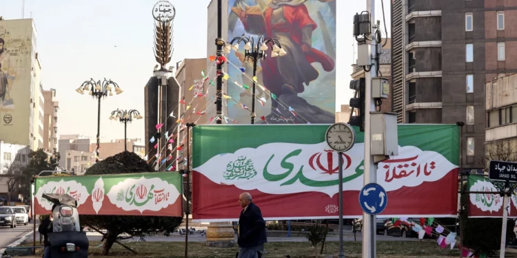 Banderas con los colores de la bandera iraní adornan una rotonda mientras un hombre pasa por delante en la capital iraní, Teherán, el 31 de enero de 2026, antes del 47.º aniversario de la Revolución Islámica de 1979. (Foto de Atta KENARE / AFP)