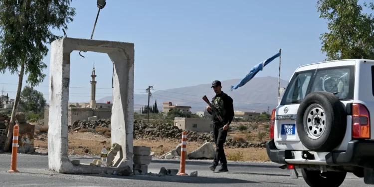 Un vehículo de la Fuerza de las Naciones Unidas para la Separación (FNUOS) pasa junto a un miembro de las fuerzas de seguridad sirias que hace guardia en el exterior de una antigua base militar cerca de la ciudad de Quneitra, en el sur de Siria, en el límite de los Altos del Golán, el 21 de septiembre de 2025 (LOUAI BESHARA / AFP)