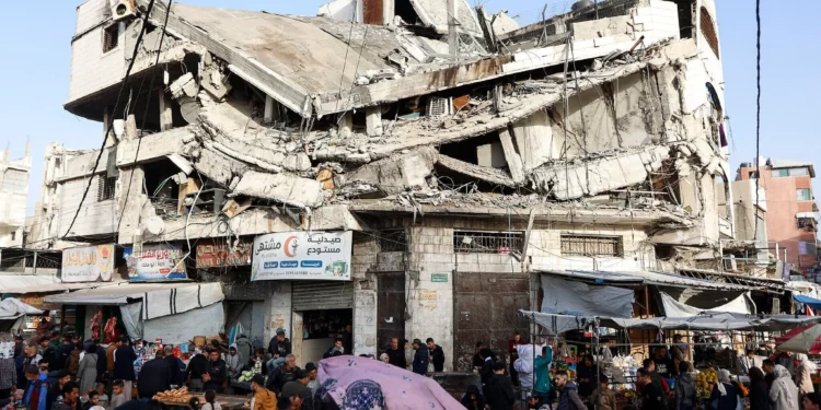 Gente compra alimentos bajo un edificio destruido en el mercado Zawiya de la ciudad de Gaza el 18 de febrero de 2026, en los primeros días del mes de ayuno del Ramadán. (Omar AL-QATTAA / AFP)