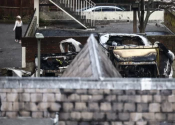 Una mujer camina junto a unas ambulancias dañadas y calcinadas (a la derecha) en la zona de Golders Green, al norte de Londres, el 23 de marzo de 2026, después de que durante la noche se incendiaran unas ambulancias de voluntarios gestionadas por una organización judía. (Foto de Henry NICHOLLS / AFP)