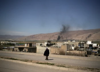Un hombre camina por una carretera mientras el humo se eleva tras los ataques perpetrados a primera hora de la mañana en una base aérea cercana en Basirma, Irak, el 12 de marzo de 2026. (AP/Leo Correa)