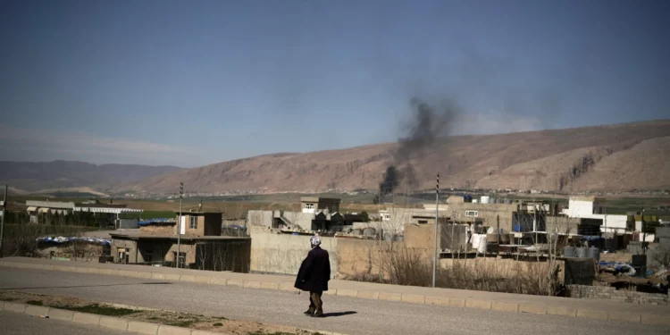 Un hombre camina por una carretera mientras el humo se eleva tras los ataques perpetrados a primera hora de la mañana en una base aérea cercana en Basirma, Irak, el 12 de marzo de 2026. (AP/Leo Correa)