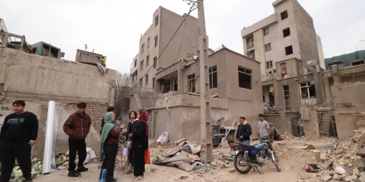 Los iraníes se reúnen frente a edificios destruidos tras un ataque militar contra la capital iraní, Teherán, el 15 de marzo de 2026. (Atta KENARE / AFP) /