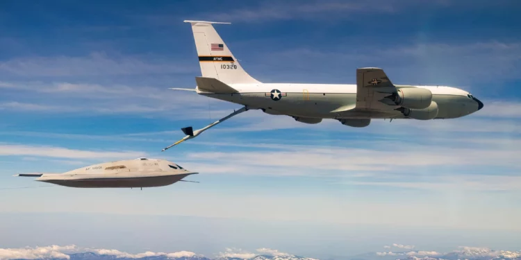 Dentro de su campaña de ensayos en la Base Aérea de Edwards, la Fuerza Aérea de EE. UU. confirmó el 14 de abril de 2026 que el B-21 Raider completó con éxito operaciones de reabastecimiento en vuelo. El avance refuerza la capacidad de ataque de largo alcance del nuevo bombardero estratégico y marca un paso relevante antes de su futura entrada en servicio dentro de la estructura de disuasión estadounidense. Las pruebas, ejecutadas junto con Northrop Grumman, forman parte del programa de evaluación con el que Washington busca validar la resistencia, el alcance global y la envolvente de rendimiento de la aeronave. Según la información oficial difundida con imágenes de los ensayos, la integración del reabastecimiento en vuelo busca reducir riesgos técnicos y acelerar el desarrollo sin renunciar a la madurez del sistema antes de su incorporación operativa. En el centro de esta fase aparece el KC-135 Stratotanker, el avión cisterna empleado para transferir combustible al Raider durante vuelos de larga duración. Ese aparato puede mover más de 90.000 kilogramos de combustible, según la configuración de la misión, y extiende la permanencia en el aire para sostener perfiles de ataque de largo alcance. En el B-21, la conexión se efectúa mediante un receptáculo dorsal ubicado detrás de la cabina. Las imágenes divulgadas muestran una compuerta de dos piezas tipo concha en esa zona, una solución distinta al sistema giratorio del B-2 Spirit. Esa disposición apunta a cambios dirigidos a reducir la firma de radar sin sumar complejidad mecánica. El avance llega además en un programa de pruebas y desarrollo concurrentes, mientras la Fuerza Aérea subraya el uso de ingeniería digital y procesos modernos de producción para acortar plazos de entrega. Durante esta fase de pruebas, las fotografías difundidas también revelan detalles de la configuración del bombardero. En ellas aparecen puertos de datos de aire delante de la cabina, característicos de la instrumentación de vuelos iniciales, además de tomas de aire con una geometría que parece optimizada para equilibrar sigilo y eficiencia de los motores. Esos rasgos refuerzan la orientación técnica del programa hacia un perfil de baja observabilidad. El B-21 retoma la arquitectura de ala volante introducida por el B-2, pero incorpora mejoras en el modelado de la sección transversal radar, materiales absorbentes de radar actualizados y estructuras compuestas. Su tamaño, ligeramente menor, apunta a reducir costos y mejorar la maniobrabilidad sin sacrificar la baja observabilidad frente a un amplio espectro de radares. La Fuerza Aérea sostiene además que consume bastante menos que el B-1B Lancer y el B-52H Stratofortress. Esa reducción de consumo, según funcionarios estadounidenses, tiene un efecto directo sobre el empleo operativo porque disminuye la dependencia de una flota limitada de aviones cisterna y libera más recursos de reabastecimiento para otros teatros. La aeronave estaría propulsada por dos motores optimizados para el sigilo, probablemente derivados de la familia Pratt & Whitney F-135, con un empuje superior a 11.000 kilogramos por unidad y firmas infrarroja y radar contenidas. Con esa configuración, el aparato tendría una velocidad de crucero cercana a 870 kilómetros por hora y una máxima próxima a 1.050 kilómetros por hora. Su alcance estimado ronda los 12.000 kilómetros y la carga útil se sitúa entre 12 y 13 toneladas. Con esas cifras, el B-21 ha sido concebido para ejecutar misiones intercontinentales con elevada autonomía, en coherencia con operaciones de penetración en entornos disputados y con su papel en la disuasión estratégica. En el plano del armamento, el bombardero mantendrá un doble cometido convencional y nuclear. Podrá transportar bombas gravitatorias nucleares B61 y B83, además del misil de crucero nuclear Long Range Stand Off. Para misiones convencionales, se prevé su compatibilidad con JDAM, JASSM y la GBU-57 Massive Ordnance Penetrator, destinada al ataque contra objetivos enterrados y fuertemente protegidos dentro de escenarios de alta complejidad defensiva. Las bodegas internas también han sido concebidas para admitir sistemas futuros, entre ellos armas hipersónicas, dentro de un enfoque centrado en la adaptabilidad. Esa lógica alcanza igualmente a la aviónica y al software. El B-21 integra fusión multisensor para combinar datos de radar, infrarrojos y guerra electrónica en un único cuadro operativo, mientras su arquitectura abierta permitiría incorporar nuevas capacidades con menos modificaciones estructurales a lo largo de su vida útil. La suite de guerra electrónica del Raider ha sido diseñada para interferir y degradar sistemas de defensa antiaérea enemigos, incluidas redes modernas de misiles tierra-aire, con el objetivo de aumentar la supervivencia del avión en escenarios de alta amenaza. En paralelo, el componente industrial del programa gana ritmo: la Fuerza Aérea mantiene como meta oficial una flota de al menos 100 aparatos y la capacidad de producción aumentó en torno a un 25 por ciento. El calendario vigente sitúa la capacidad operativa inicial en torno a 2027. Las primeras aeronaves destinadas al servicio deberían llegar a la Base Aérea de Ellsworth, en Dakota del Sur, donde ya se ejecutan trabajos de infraestructura y ajustes de pista e instalaciones para sistemas de baja observabilidad. Frente al número reducido de B-2 Spirit y a la falta de características furtivas del B-52H, el Raider ampliará las opciones de ataque de largo alcance de EE. UU.