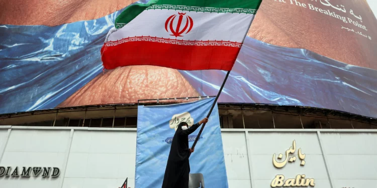 Una mujer ondea una bandera iraní frente a una valla publicitaria antiestadounidense que hace referencia al presidente estadounidense Donald Trump y al Estrecho de Ormuz en la Plaza Valiasr, en Teherán, Irán, el 5 de mayo de 2026. (AFP)
