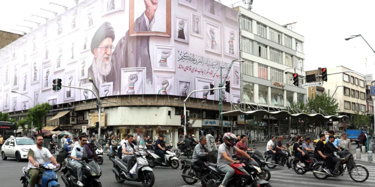 Los iraníes pasan en coche junto a una enorme valla publicitaria con la imagen del líder supremo iraní Alí Jamenei, asesinado en febrero de 2026 en un ataque militar de Estados Unidos e Israel contra Irán, en una calle de Teherán el 5 de mayo de 2026. (AFP)