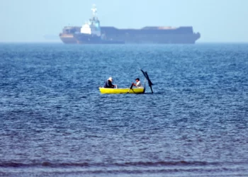 En esta imagen obtenida de la agencia de noticias iraní ISNA el 4 de mayo de 2026, se ve a dos hombres sentados en una barca pescando cerca de un buque anclado en el estrecho de Ormuz, frente a Bandar Abbas, en el sur de Irán. (Amirhossein KHORGOOEI / ISNA / AFP)