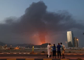 Trabajadores extranjeros observan cómo una alta columna de humo negro se eleva tras una explosión en la zona industrial de Fuyairah el 3 de marzo de 2026. (Fadel SENNA / AFP)