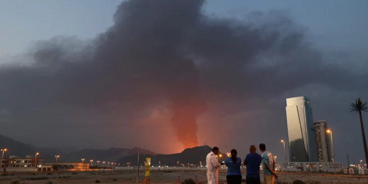 Trabajadores extranjeros observan cómo una alta columna de humo negro se eleva tras una explosión en la zona industrial de Fuyairah el 3 de marzo de 2026. (Fadel SENNA / AFP)