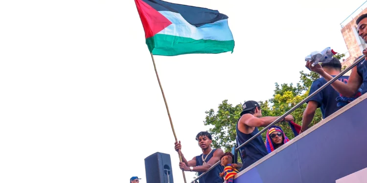 El jugador del FC Barcelona Lamine Yamal sostiene una bandera palestina mientras celebra con su equipo en lo alto de un autobús tras ganar el título de la Liga española de fútbol en Barcelona, España, el 11 de mayo de 2026. (Foto AP)