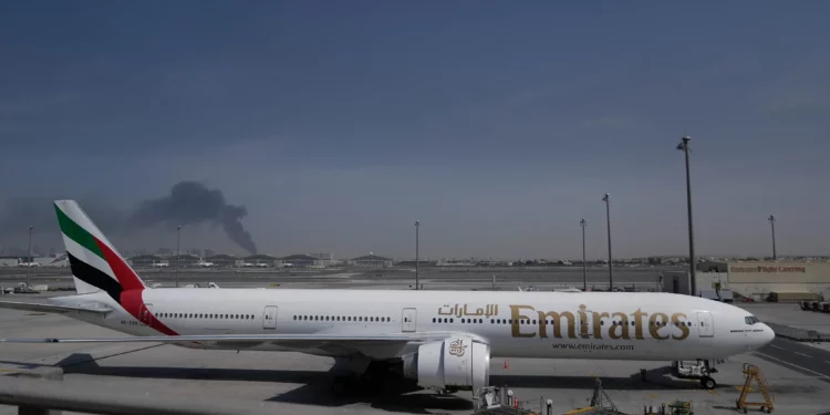 Se observa una columna de humo provocada por un ataque iraní al fondo, mientras un avión de Emirates permanece estacionado en el Aeropuerto Internacional de Dubái tras su cierre, en Dubái, Emiratos Árabes Unidos, el 1 de marzo de 2026. (Foto AP/Altaf Qadri)
